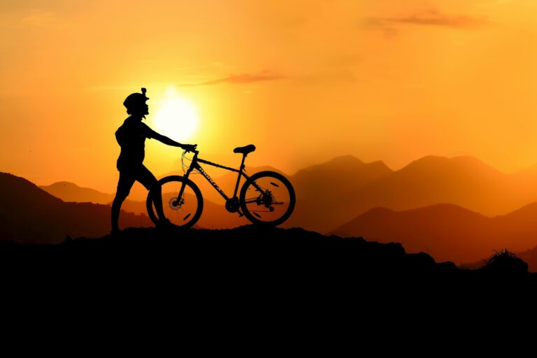 Silhouette of cyclist on top of hill in sunset with cycling gear