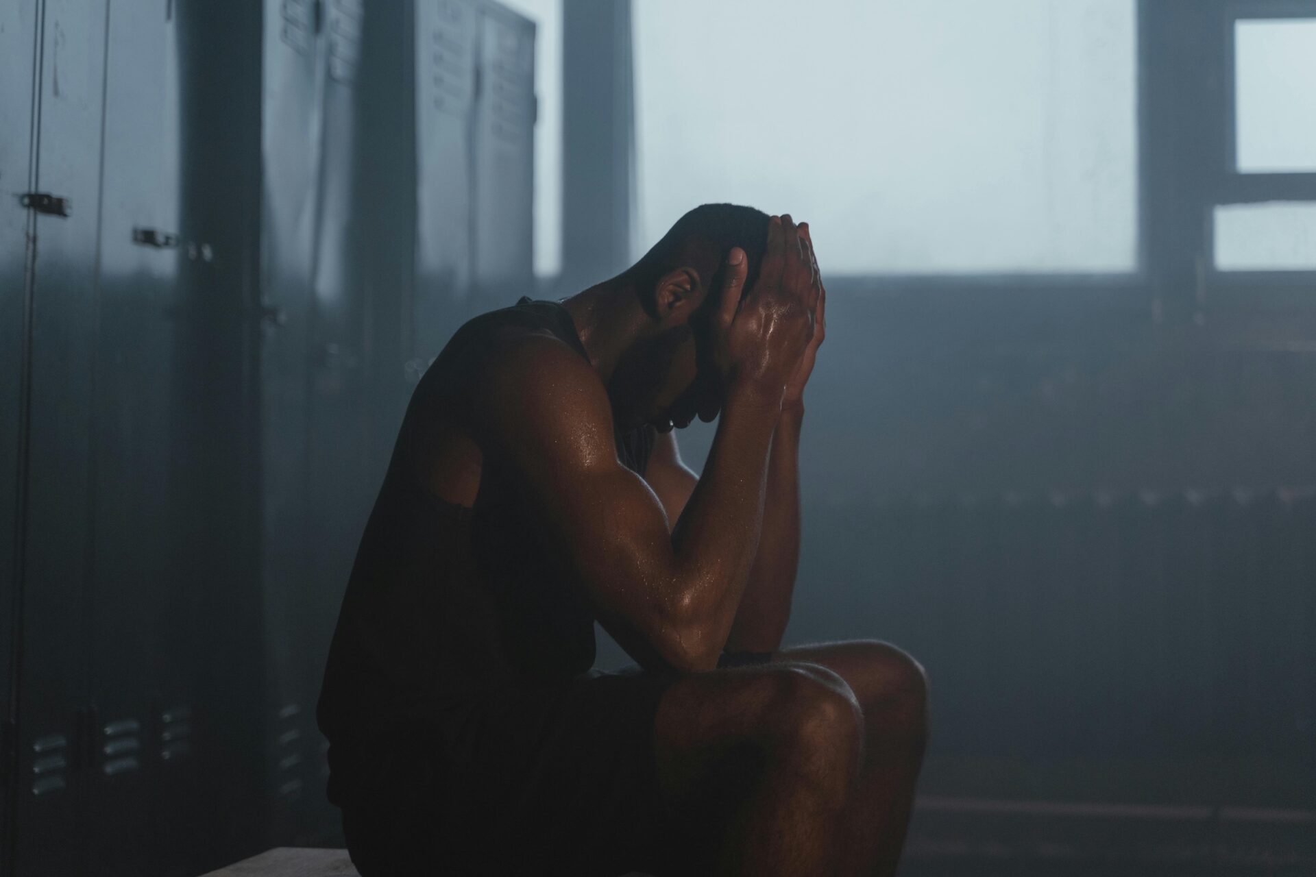 Sweaty man taking rest in gym locker room after workout