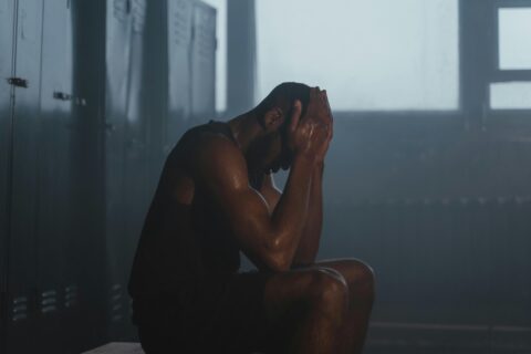 Sweaty man taking rest in gym locker room after workout