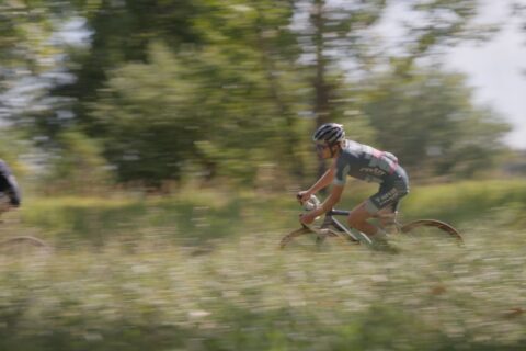 A cyclocross rider rounds a bend through tall grass for cycling thresholds
