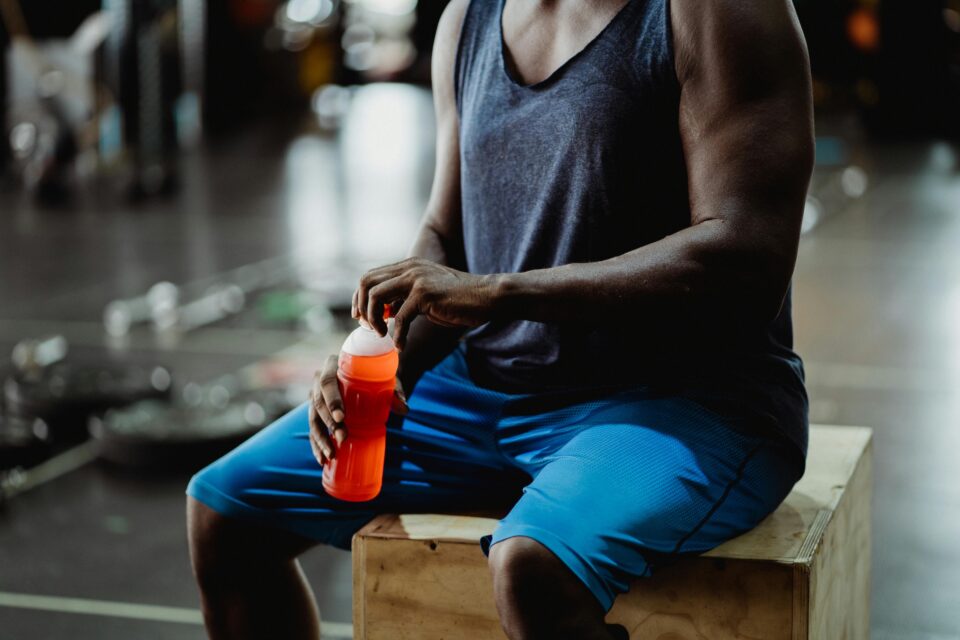 Athlete in grey tank top and blue shorts opening sports drink in gym for fasting