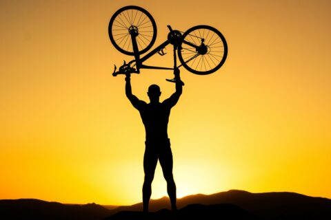 Cyclist holding bike in air in front of sunset for training and performance goals