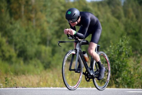 A triathlete dressed all in black grimaces while riding his bike