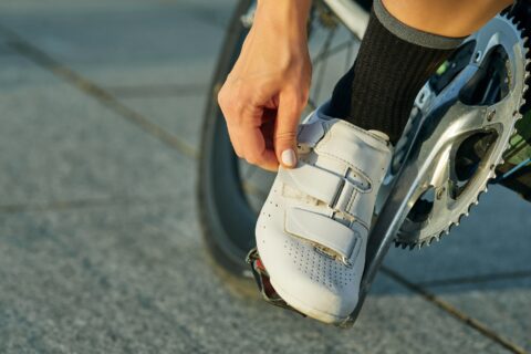 A woman tightens the strap on her white cycling cleat.