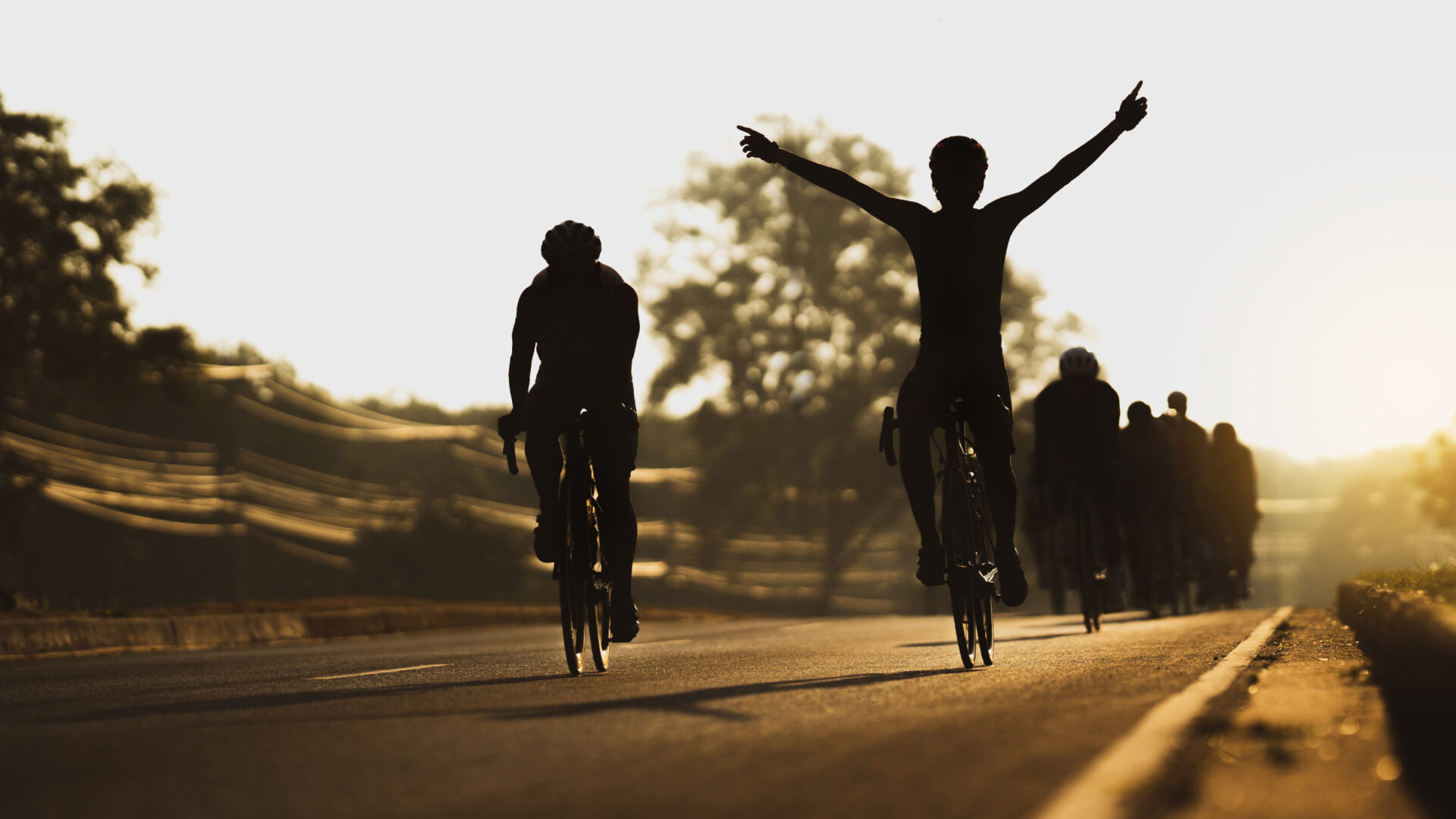 Silhouettes of cyclists riding in a group, with one holding their arms overhead