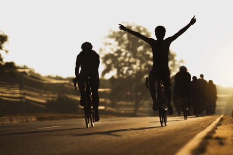 Silhouettes of cyclists riding in a group, with one holding their arms overhead