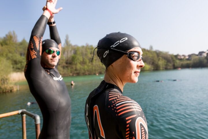 a male and a female adult triathlete wearing wetsuits and preparing to swim