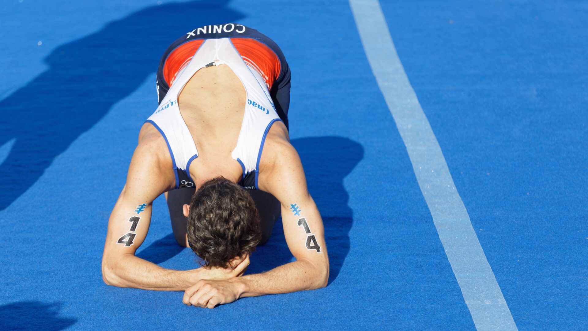 A triathlete kneels face-down on a blue track