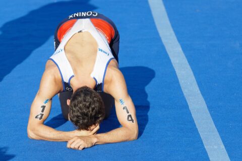 A triathlete kneels face-down on a blue track