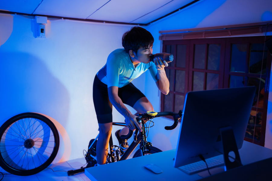 Asian man cycling on the machine trainer he is exercising in the home at night.he play online bike game