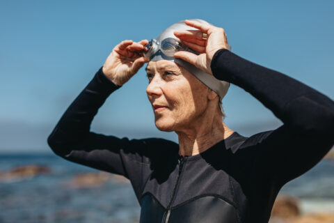 A masters athlete puts on her googles as she gets ready to swim in the ocean