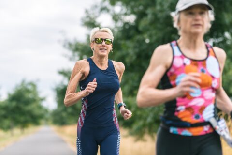 Two older women running down a trail during a triathlon