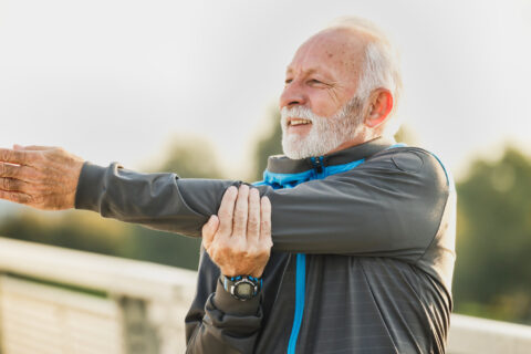 Masters runner performing an arm stretch before a run