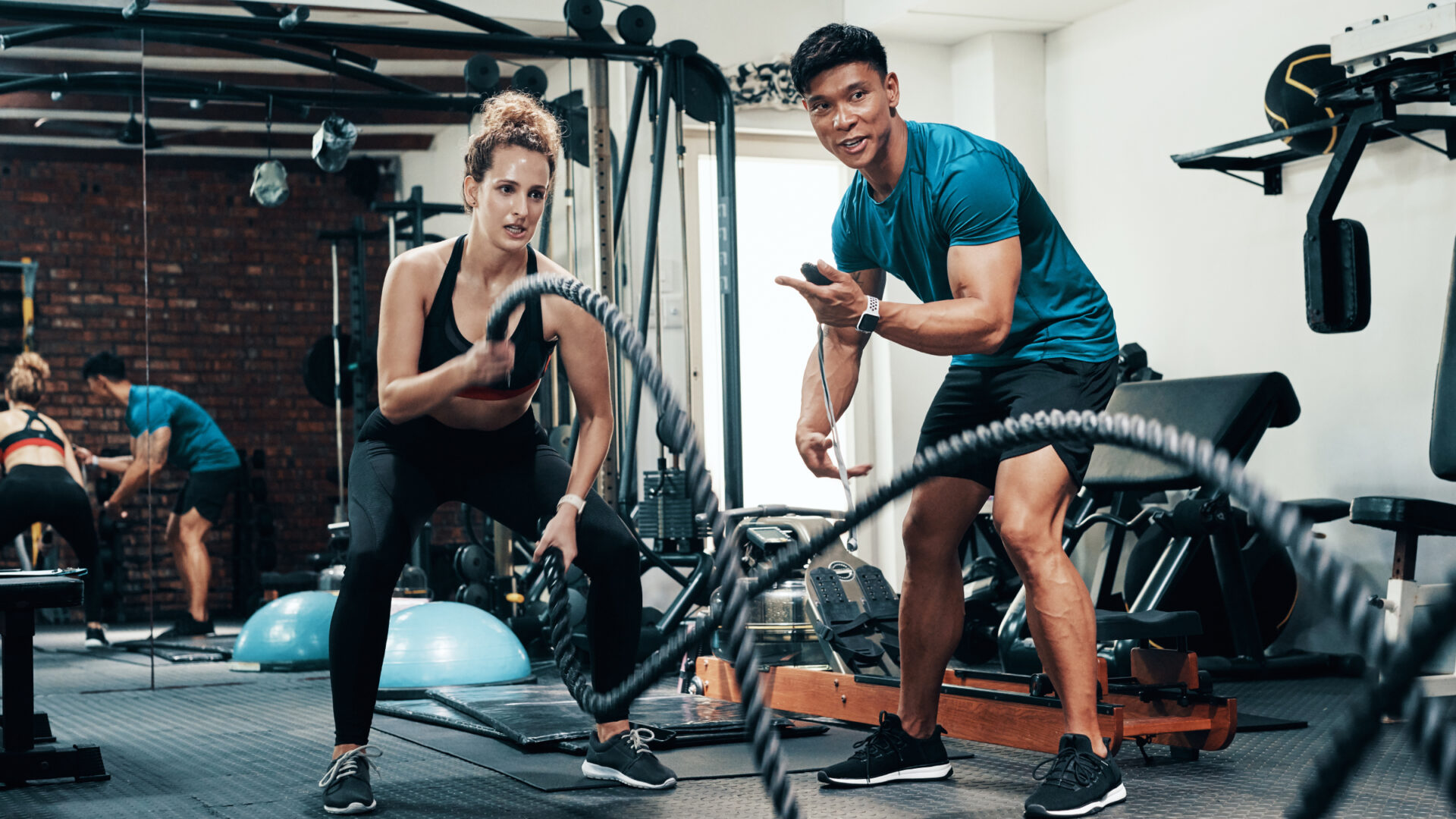 A woman exercising with battle ropes while her coach encourages her