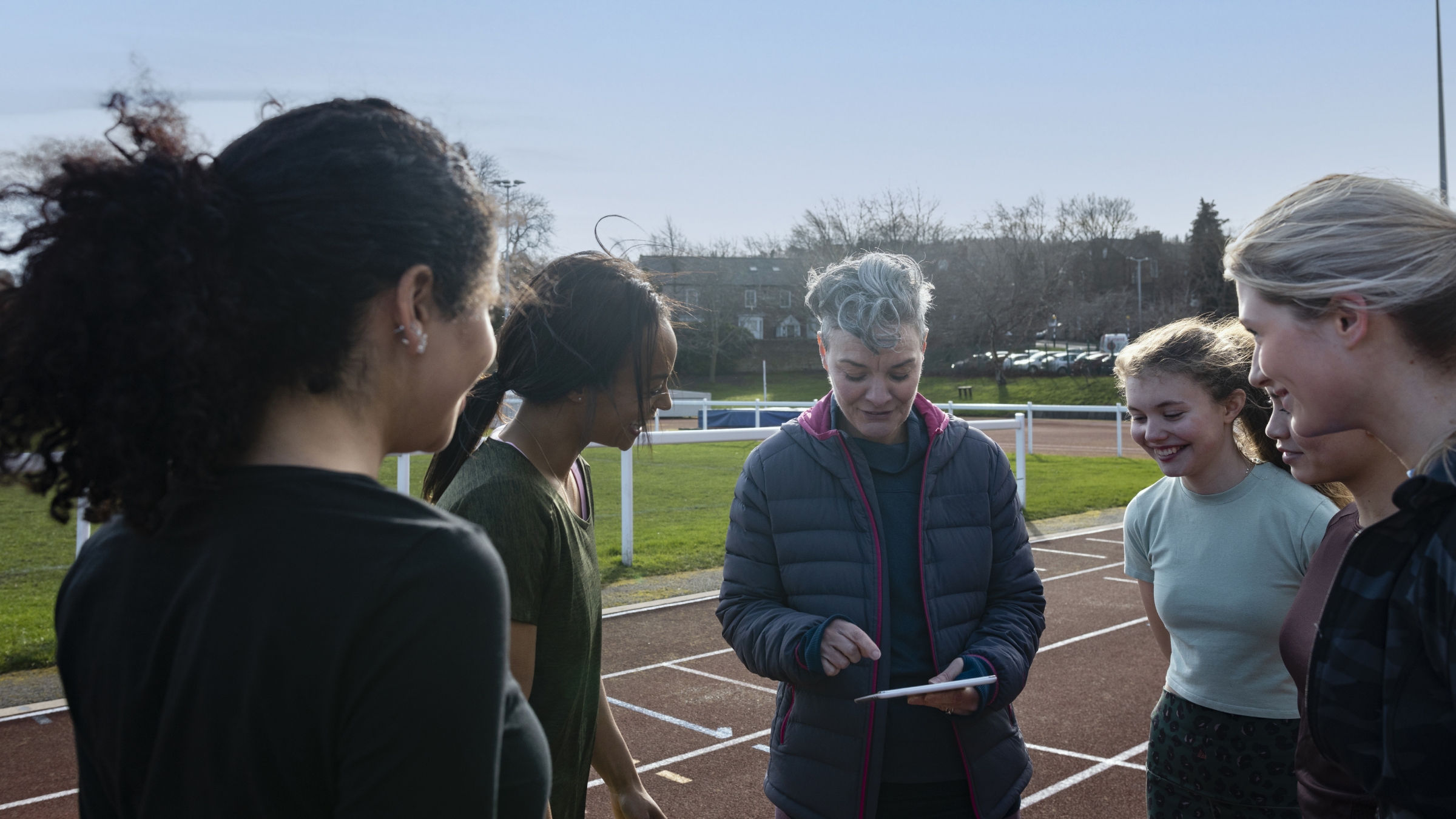 A coach and her athletes look at her tablet before running a track workout