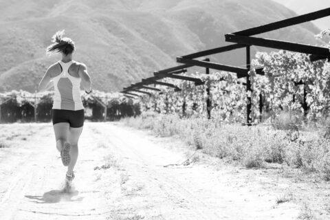 Black-and-white image of a woman running past a vineyard