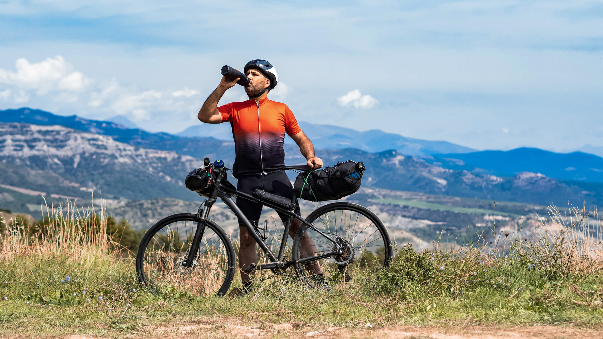 Bikepacker fueling at a ridge overlooking a small mountain range