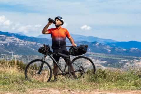 Bikepacker fueling at a ridge overlooking a small mountain range