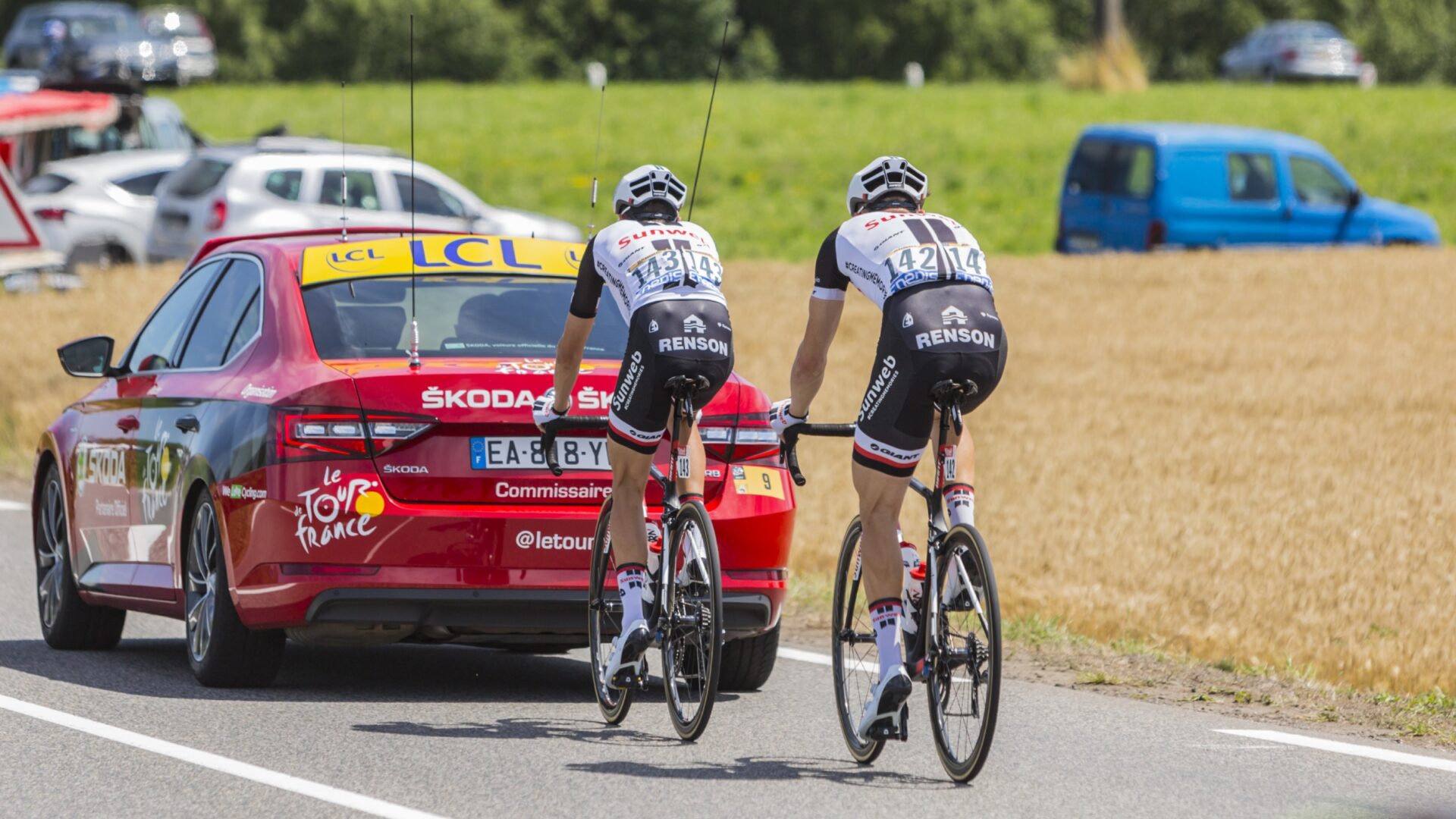 Two cyclists motor pacing behind a red car on a sunny day