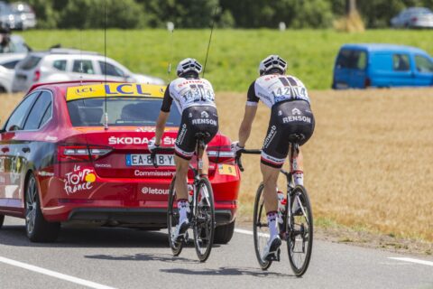 Two cyclists motor pacing behind a red car on a sunny day