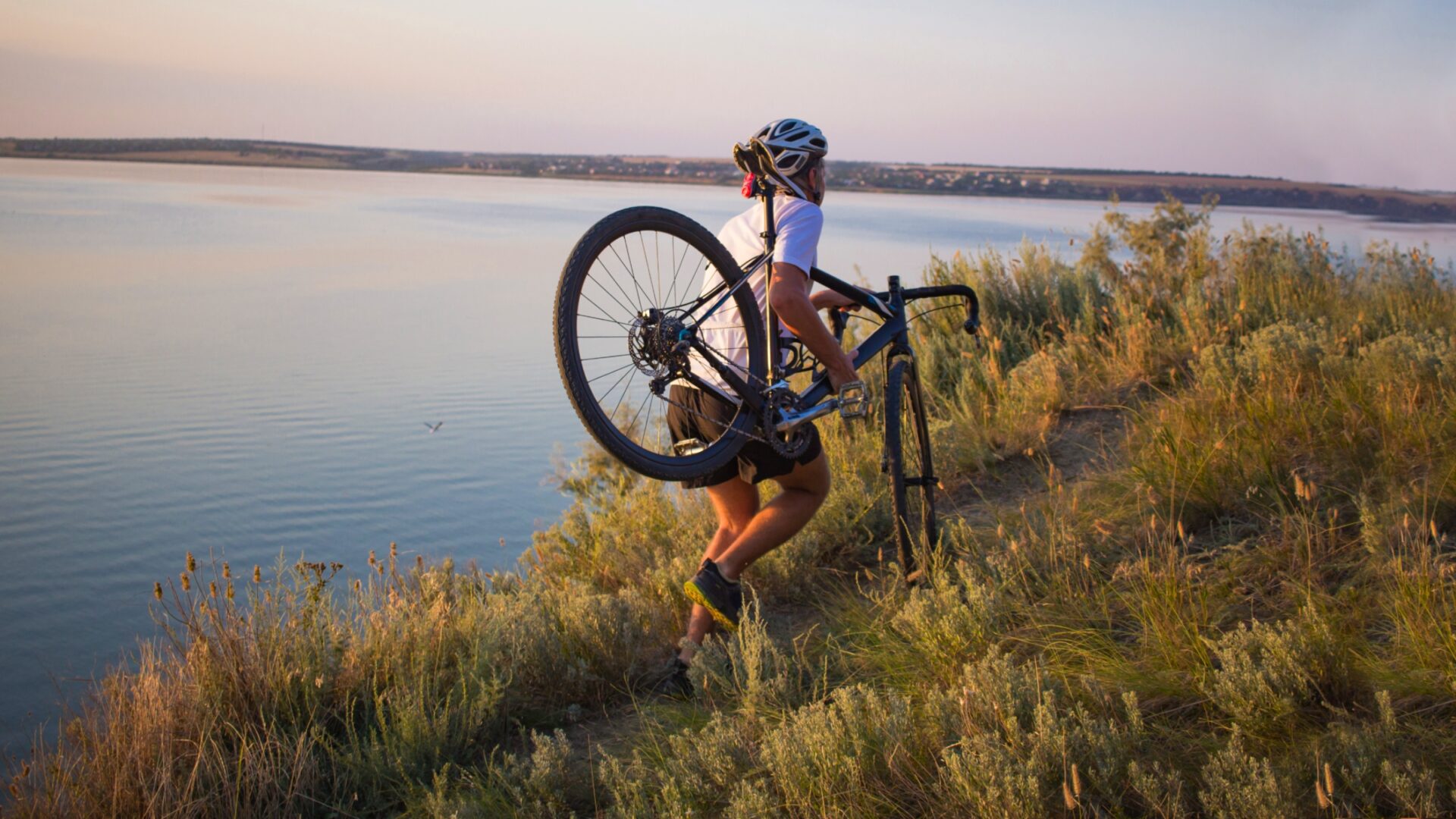 A man runs along a coastal cliff with a cyclocross bike on his shoulder