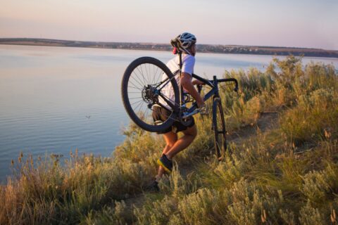 A man runs along a coastal cliff with a cyclocross bike on his shoulder