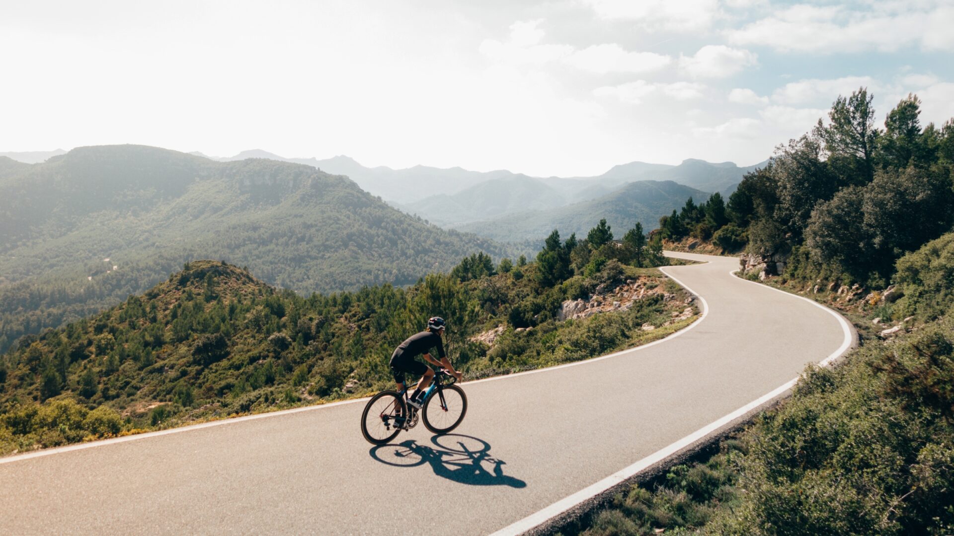 A cyclist rides along an undulating mountain road on a bright day