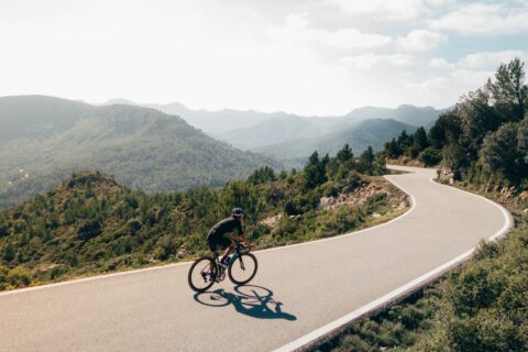 A cyclist rides along an undulating mountain road on a bright day
