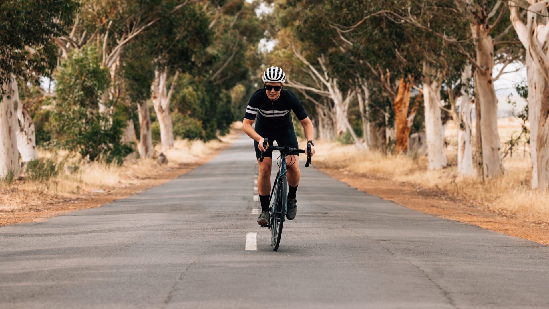 Woman riding out of the saddle along a tree-lined road, cycling toward the camera