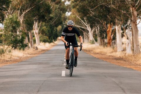 Woman riding out of the saddle along a tree-lined road, cycling toward the camera