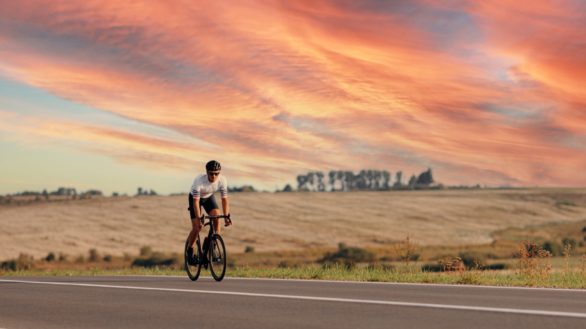 A male cyclist rides along an empty road at sunset