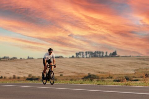 A male cyclist rides along an empty road at sunset