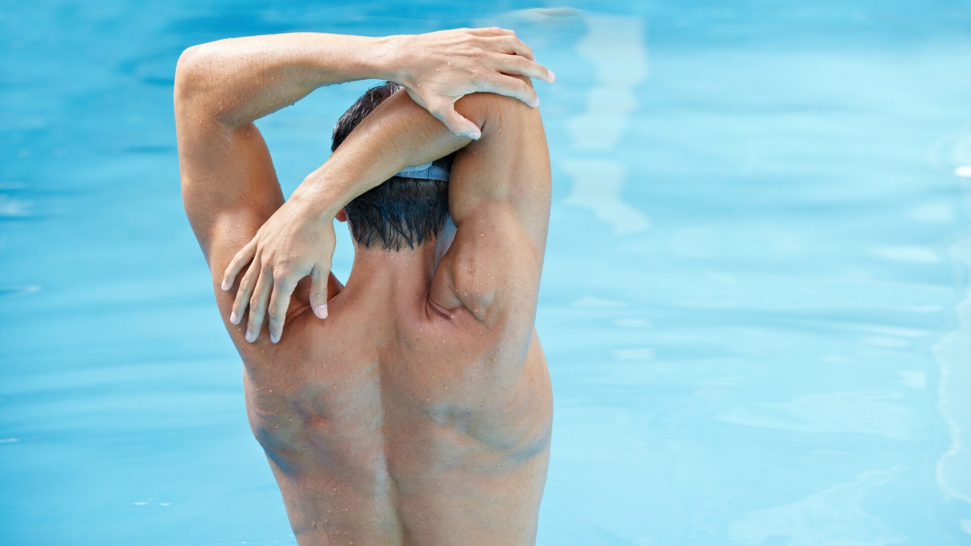 Rear view of a swimmer's upper torso while they stretch their arms behind their head.