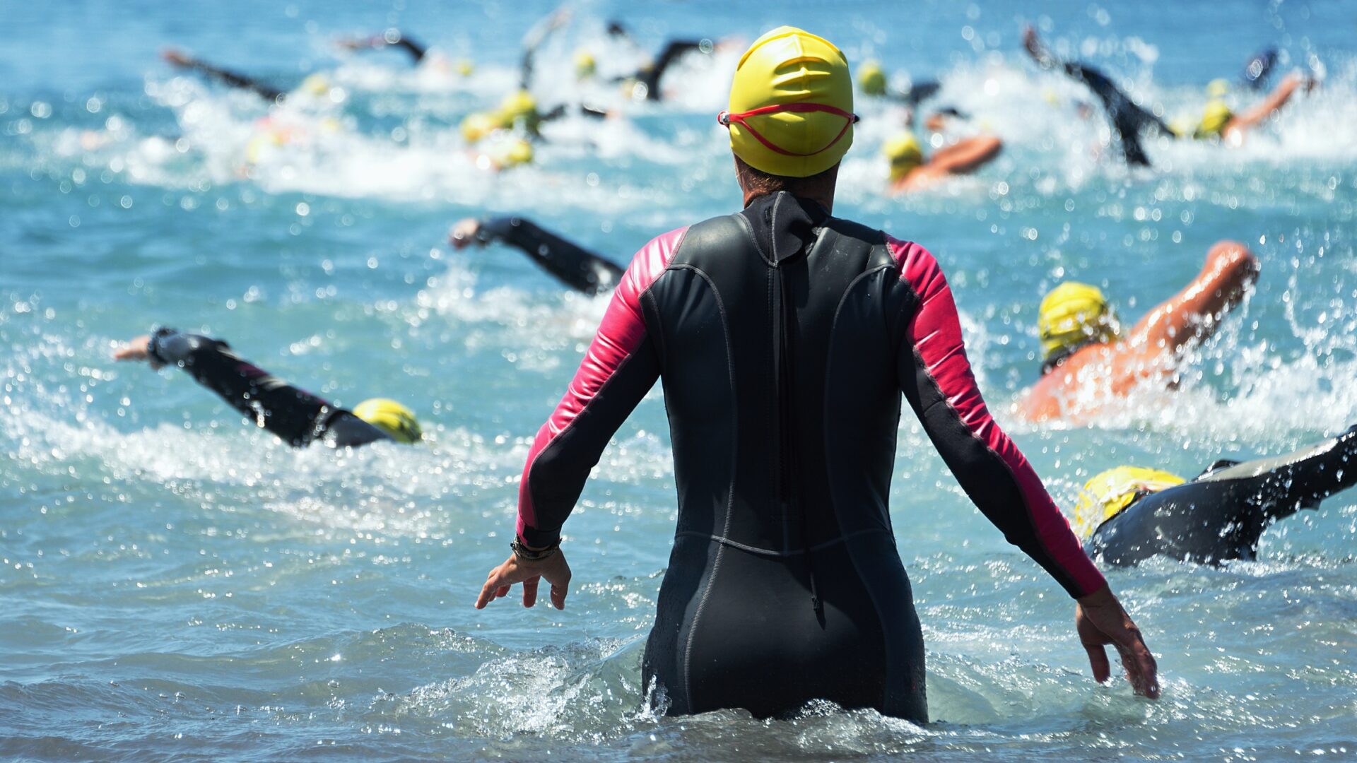 Rear shot of a woman looking out at competitors during the swim start of a triathlon.