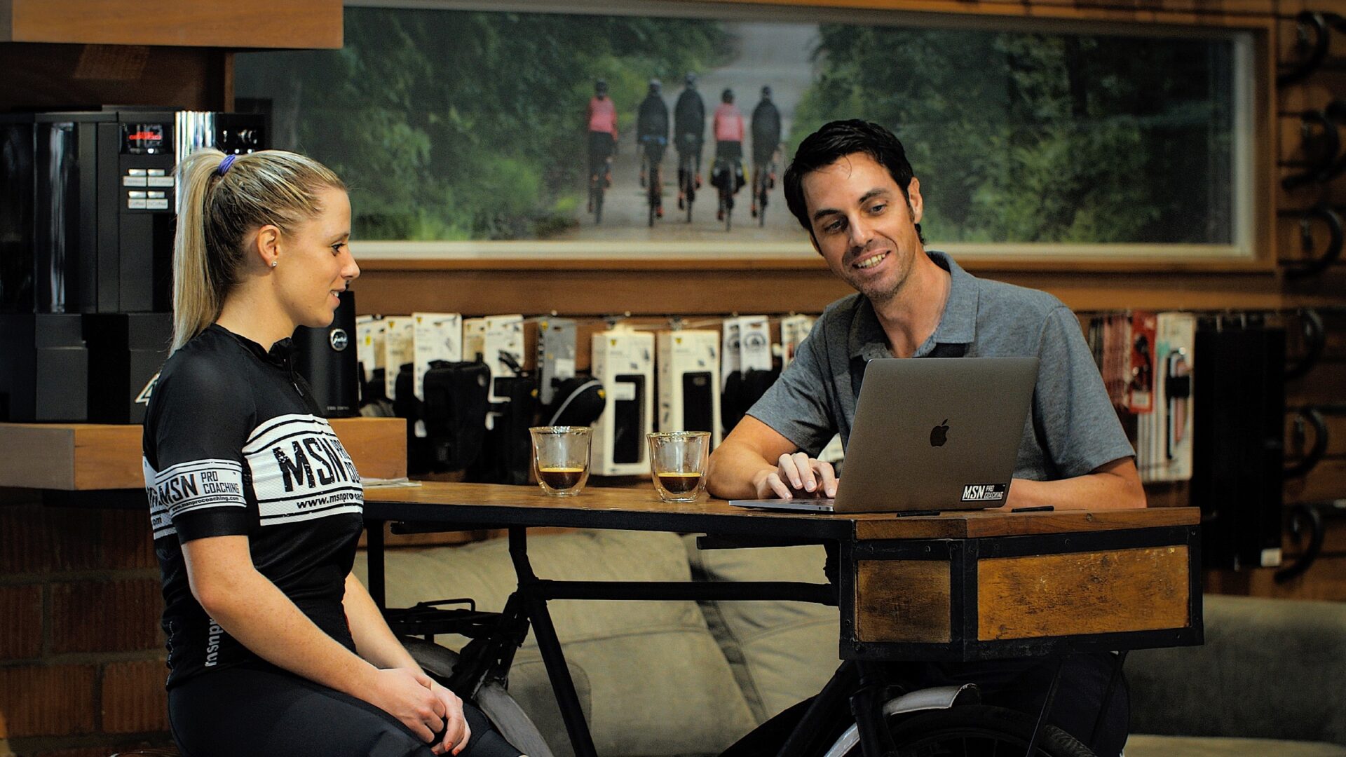 Mike Norton sitting at a table with a cyclist, showing her data on a laptop.