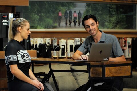 Mike Norton sitting at a table with a cyclist, showing her data on a laptop.