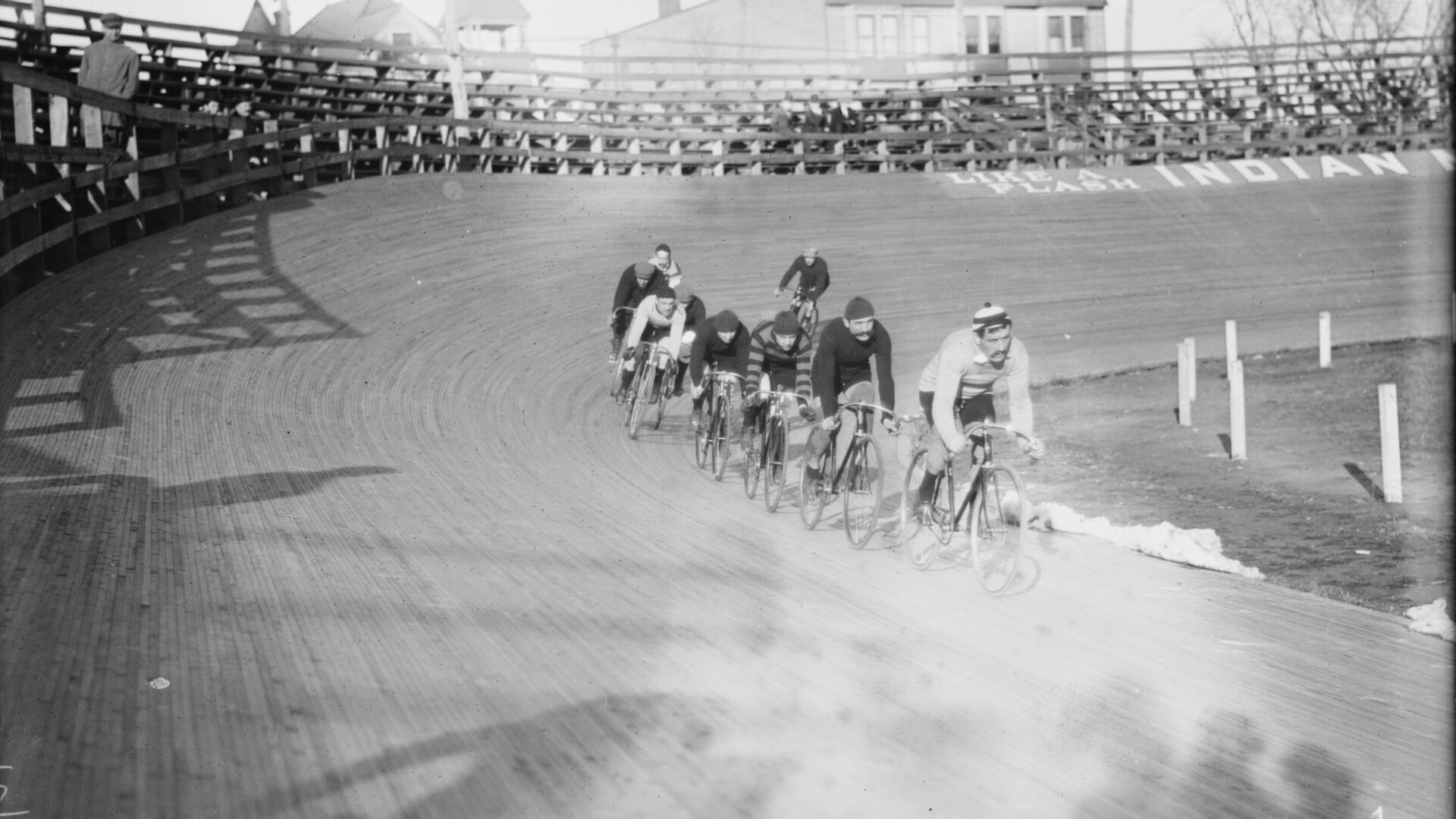 Historical black-and-white photo of cyclists racing around a velodrome