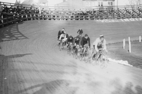 Historical black-and-white photo of cyclists racing around a velodrome