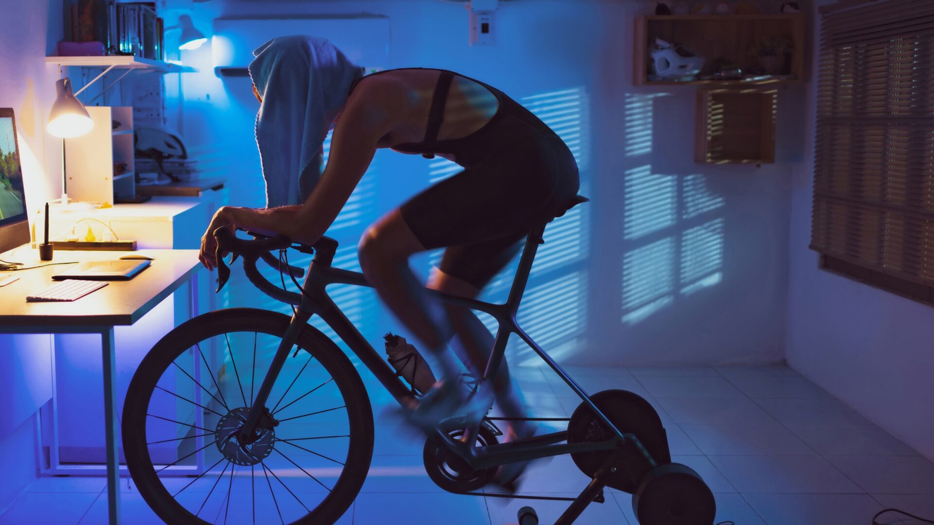 Cyclist rides on an indoor trainer in a dark room. He has his shirt covering his head