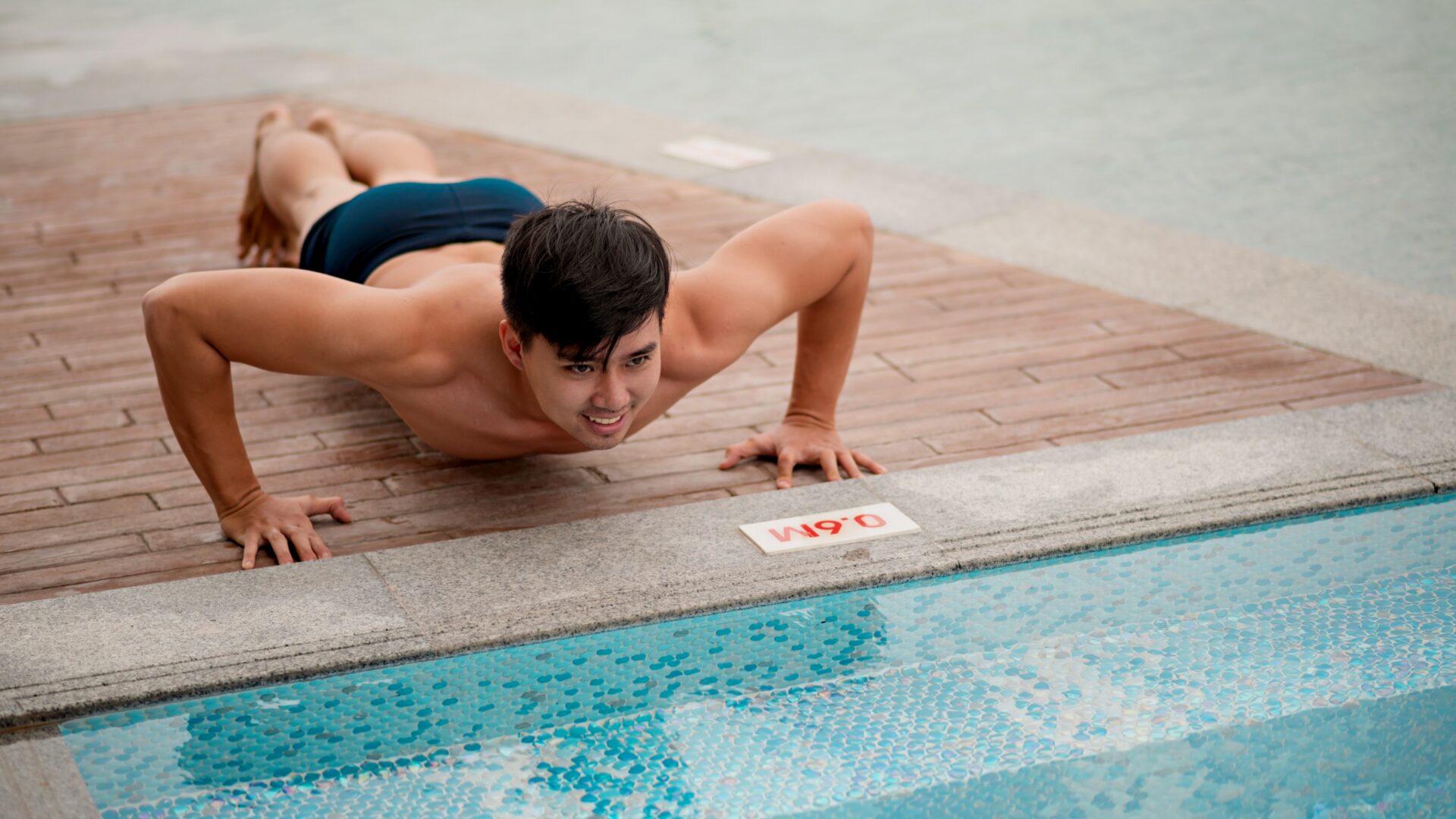 Young man doing pushups by a pool for a swim and dryland workout.