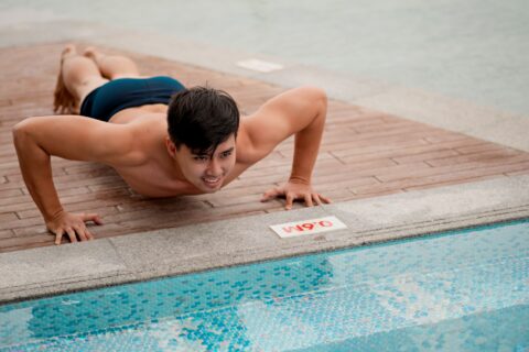 Young man doing pushups by a pool for a swim and dryland workout.