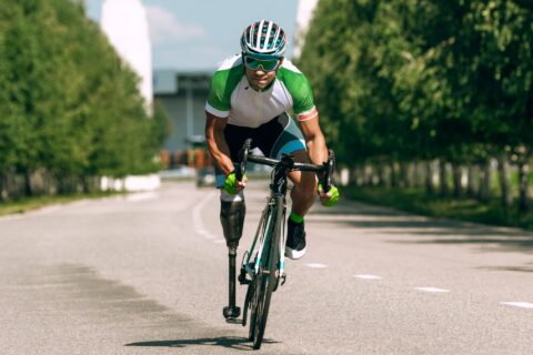 A male cyclist with a prosthetic leg rides out of the saddle toward the camera.