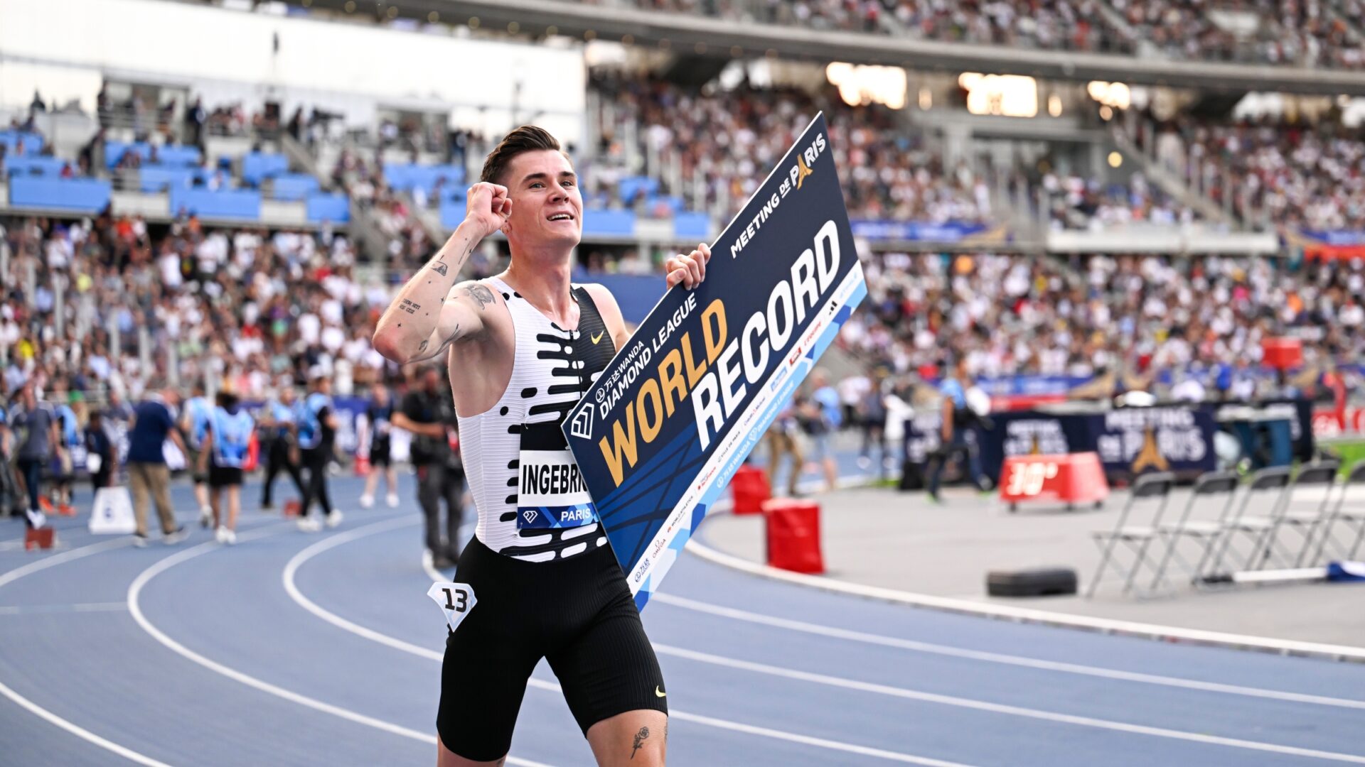 Jakob Ingebrigtsen celebrates on a running track, holding one fist in the air and displaying a "World Record" sign with the other hand.