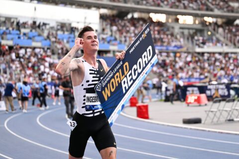 Jakob Ingebrigtsen celebrates on a running track, holding one fist in the air and displaying a "World Record" sign with the other hand.