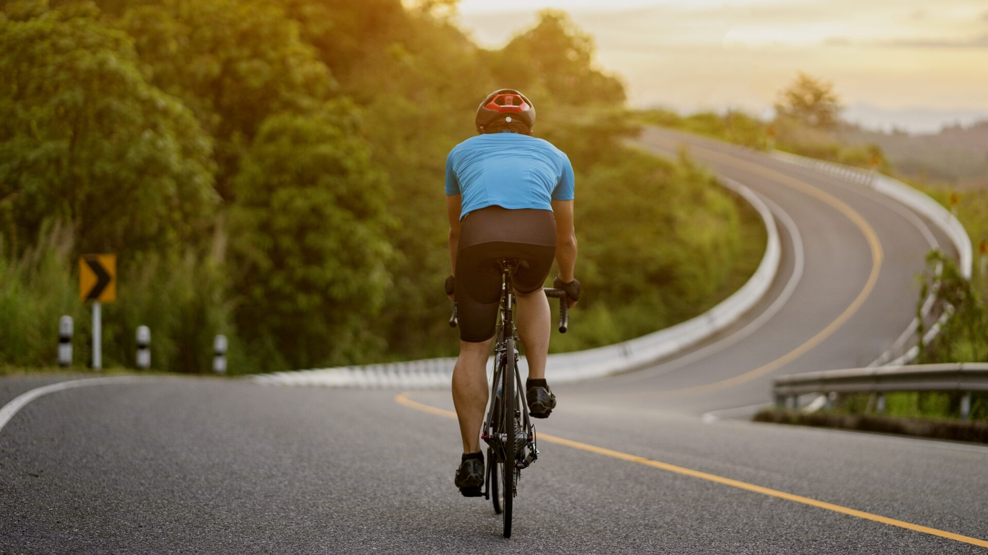 Rear shot of a cyclist riding a rolling road at sunset