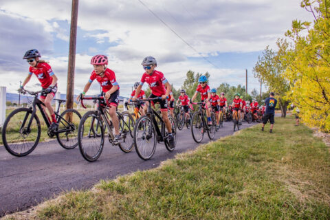 Boulder Junior Cycling youth cyclists compete during a bike race wearing their signature bright red, BJC cycling jerseys.