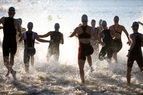 A group of women triathletes runs into the water at the beginning of the swim leg of a triathlon.