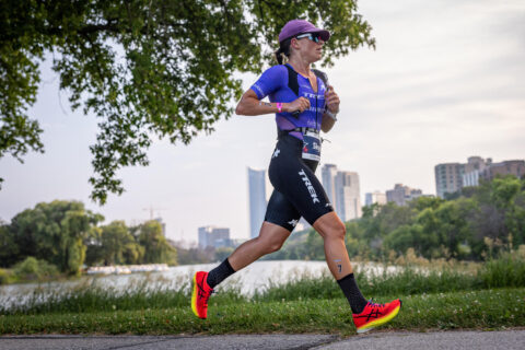 Professional triathlete Skye Moench runs in a purple triathlon race suit during a triathlon race in a city park.