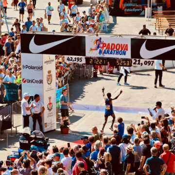 A competitive marathon runner with arms raised in the air crosses the finish line at the Padova Marathon.