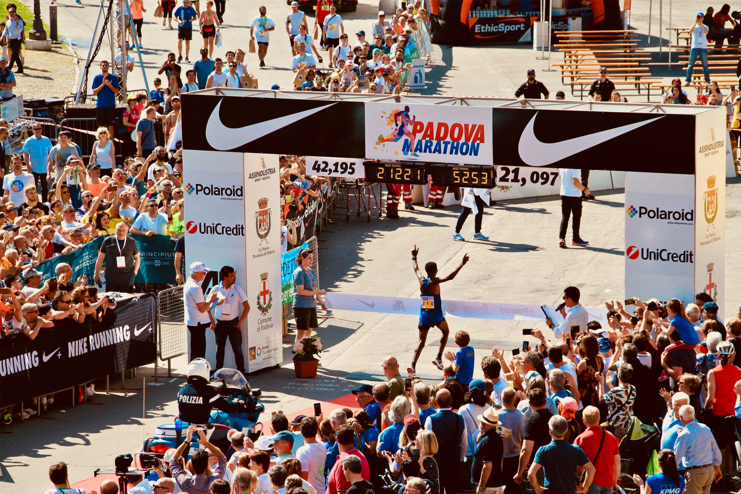 A competitive marathon runner with arms raised in the air crosses the finish line at the Padova Marathon.